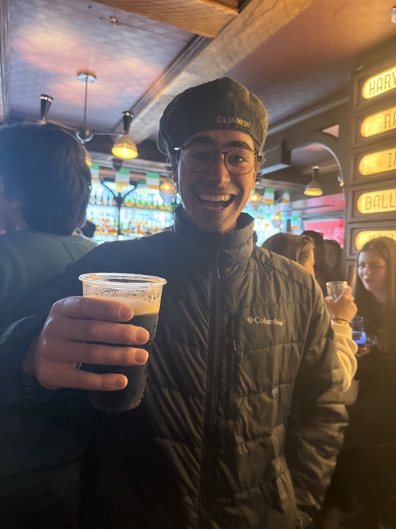 Holding a pint in a pub under neon signs.